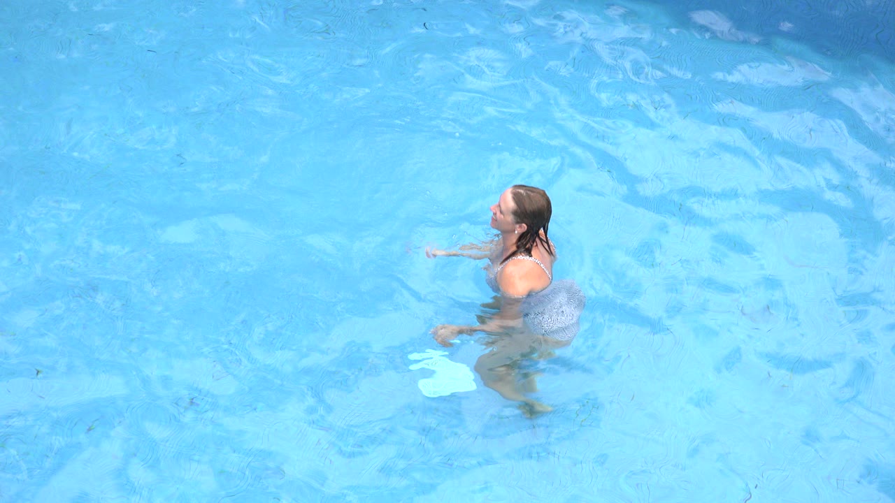 An adult woman in a swimsuit stands chest-deep in a blue pool in Los Cabos, Mexico, with rippled water filling the frame.