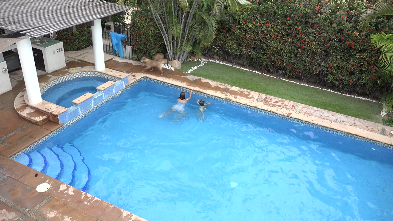 Two children swimming near an attached jacuzzi in a blue pool.