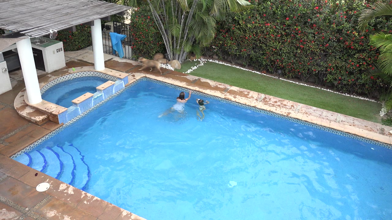 The swimmers remain near the jacuzzi side of the Los Cabos pool, with ripples spreading across the bright blue water and a covered structure at the upper left.