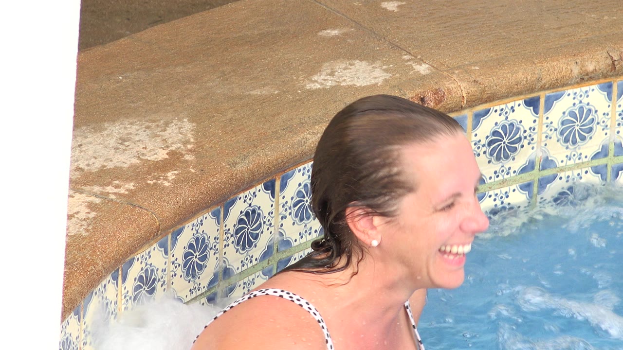 Woman smiling at the edge of a blue pool beside floral tile.