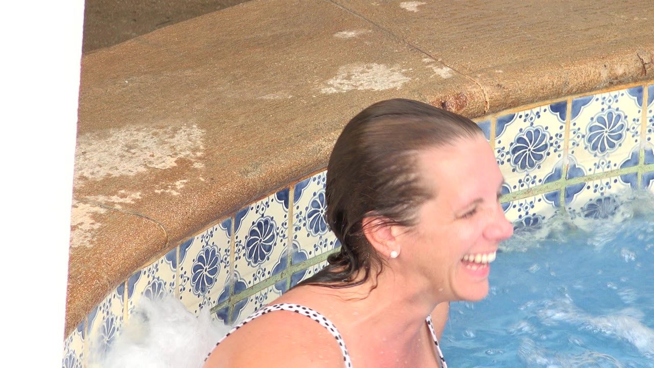 Adult woman laughs in a close view at the pool edge in Los Cabos, Mexico, as bubbling water rises near the blue floral tile.