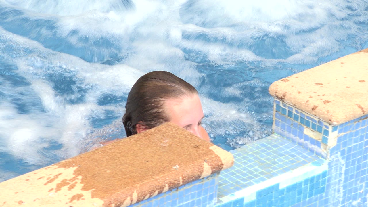 At the start of the Los Cabos clip, a woman is mostly hidden behind the tan hot tub edge while white bubbles move across the blue water.