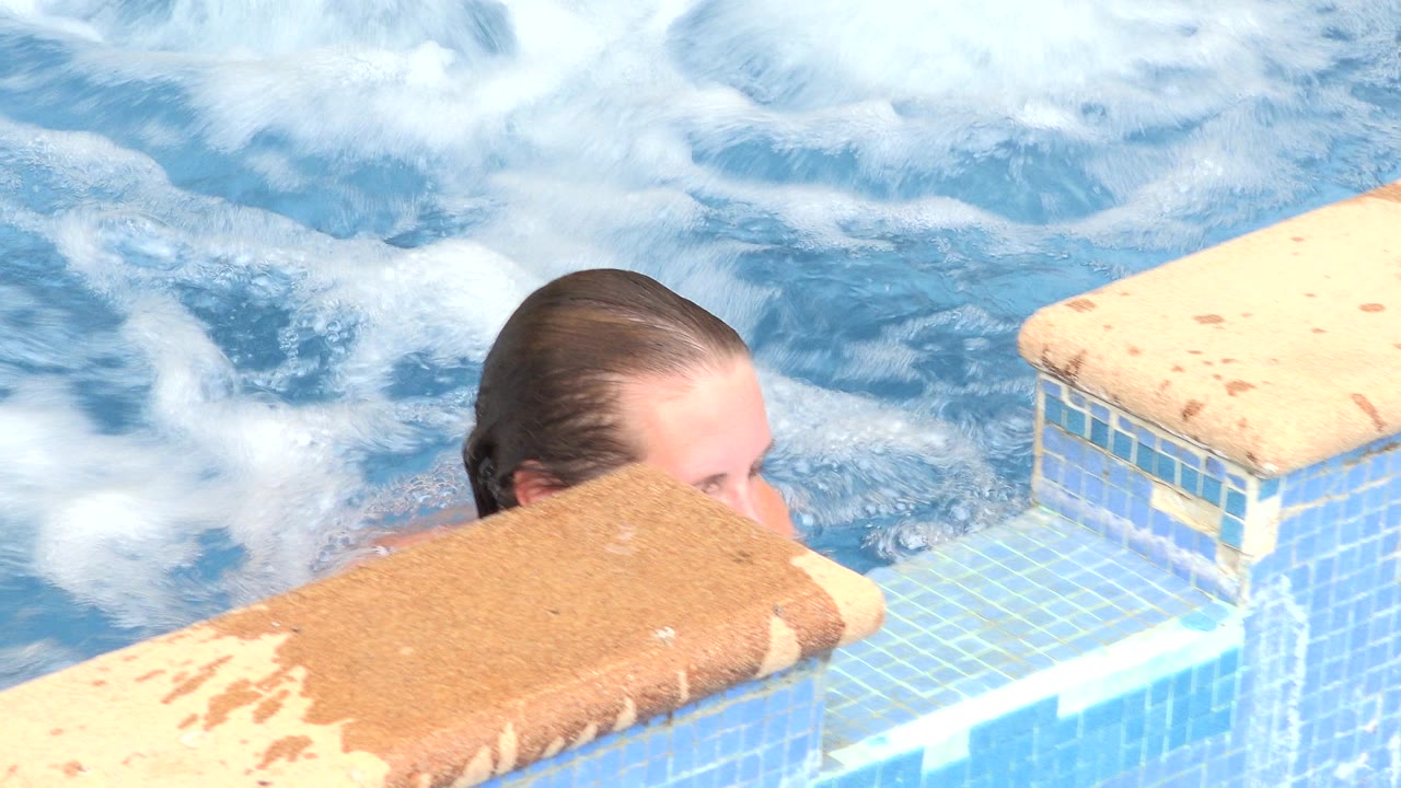 A woman in Los Cabos remains low in the hot tub, with wet hair visible above the tan ledge and foamy blue water behind her.