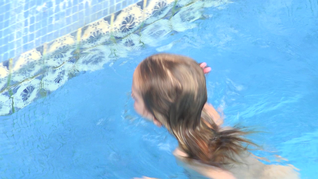 Young girl in a Los Cabos, Mexico pool swims close to a blue tiled wall, seen from above with wet hair and bright water around her.