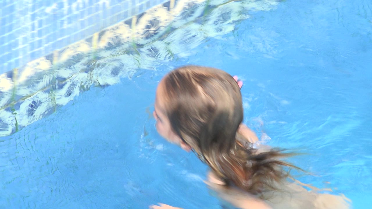 The girl remains near the tiled wall in the Los Cabos pool, with her head turned sideways and ripples trailing behind her shoulders.