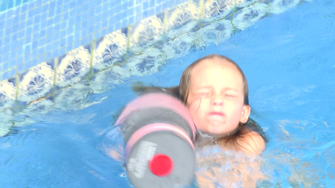 At 0:01 in Los Cabos, Mexico, the young girl has her eyes closed while the foam float sits in the foreground and patterned pool tile lines the upper edge of the frame.