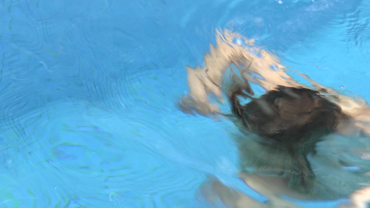 The child remains just under the water surface in Los Cabos, Mexico, with hair and shoulders blurred by a wavering patch of bright blue pool water.