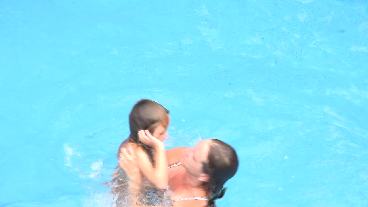 Woman holding a child in a bright blue pool.