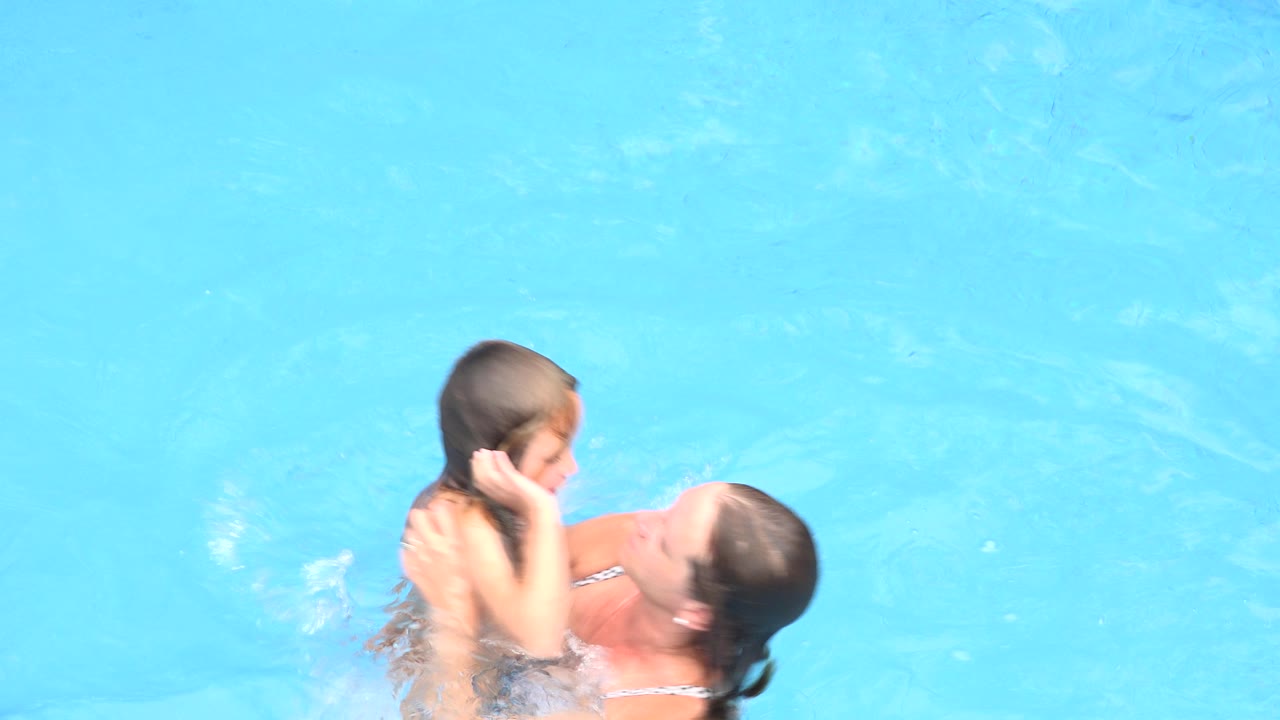The child faces the woman as she supports them in the pool, with open blue water filling the background in Los Cabos, Mexico.