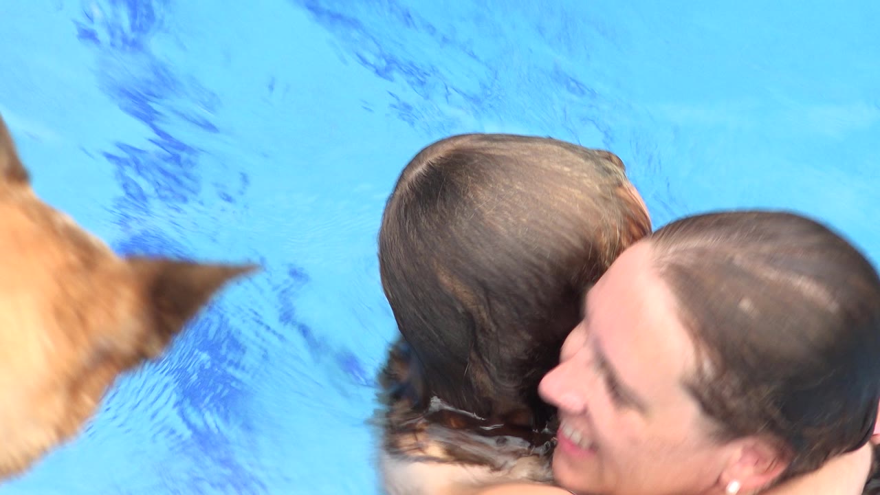 One second into the Los Cabos footage, the woman and child remain in a close embrace in blue water while the tan dog shape is still partly visible at frame left.
