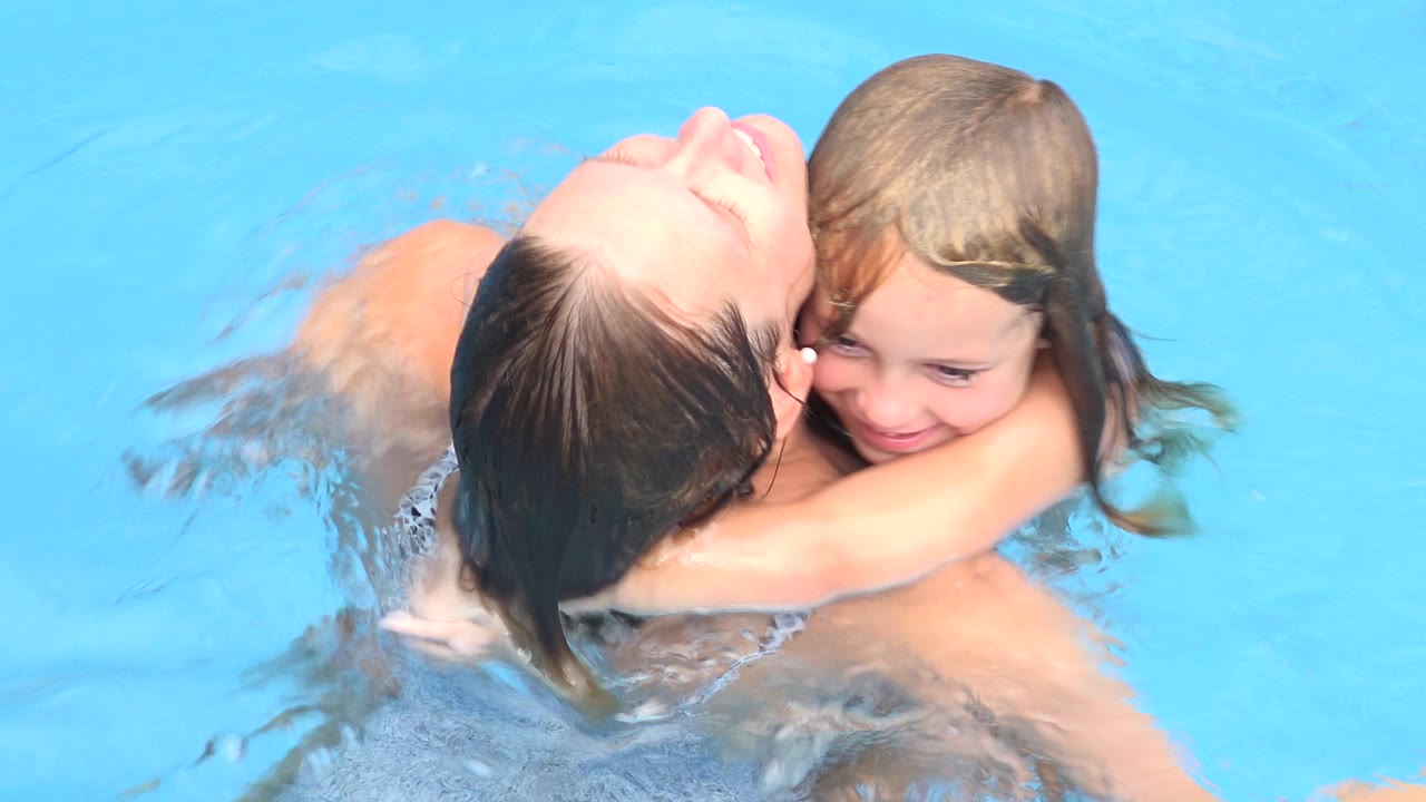 Woman holding a young girl in a bright blue swimming pool.