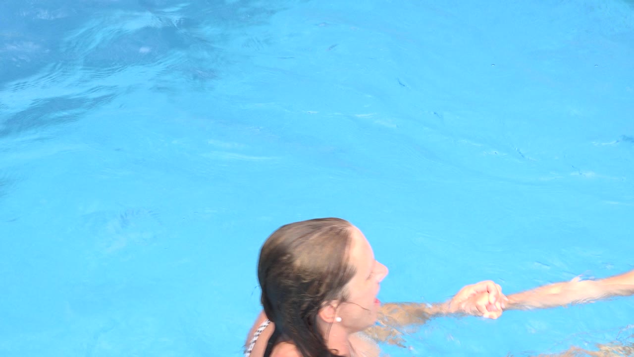 Woman in a pool holding a child's hand at the water surface.