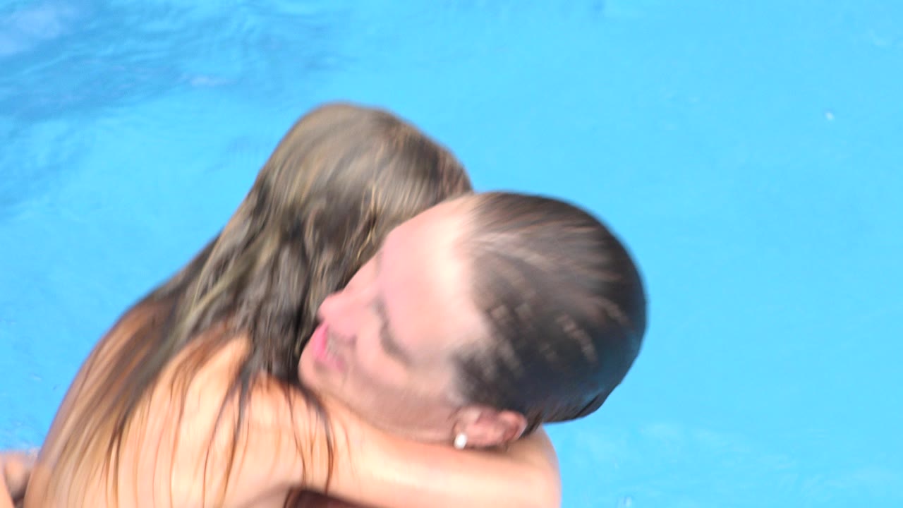 At 0:00, a mother holds her daughter close in bright blue water in Los Cabos, Mexico, with the daughter's back and the mother's face partly visible.