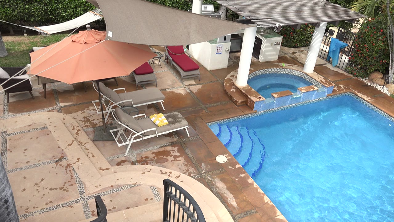 Elevated view of a hotel pool deck with loungers and hot tub.