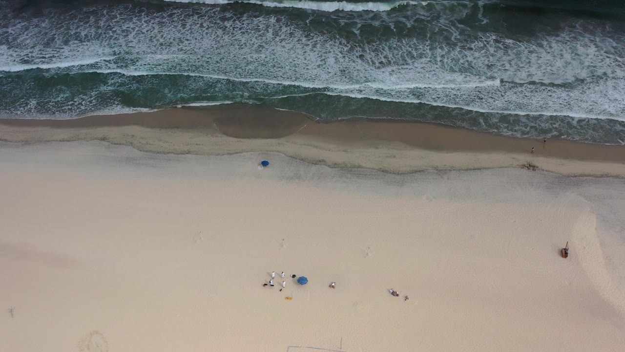 Overhead shoreline with foamy waves and pale sand.