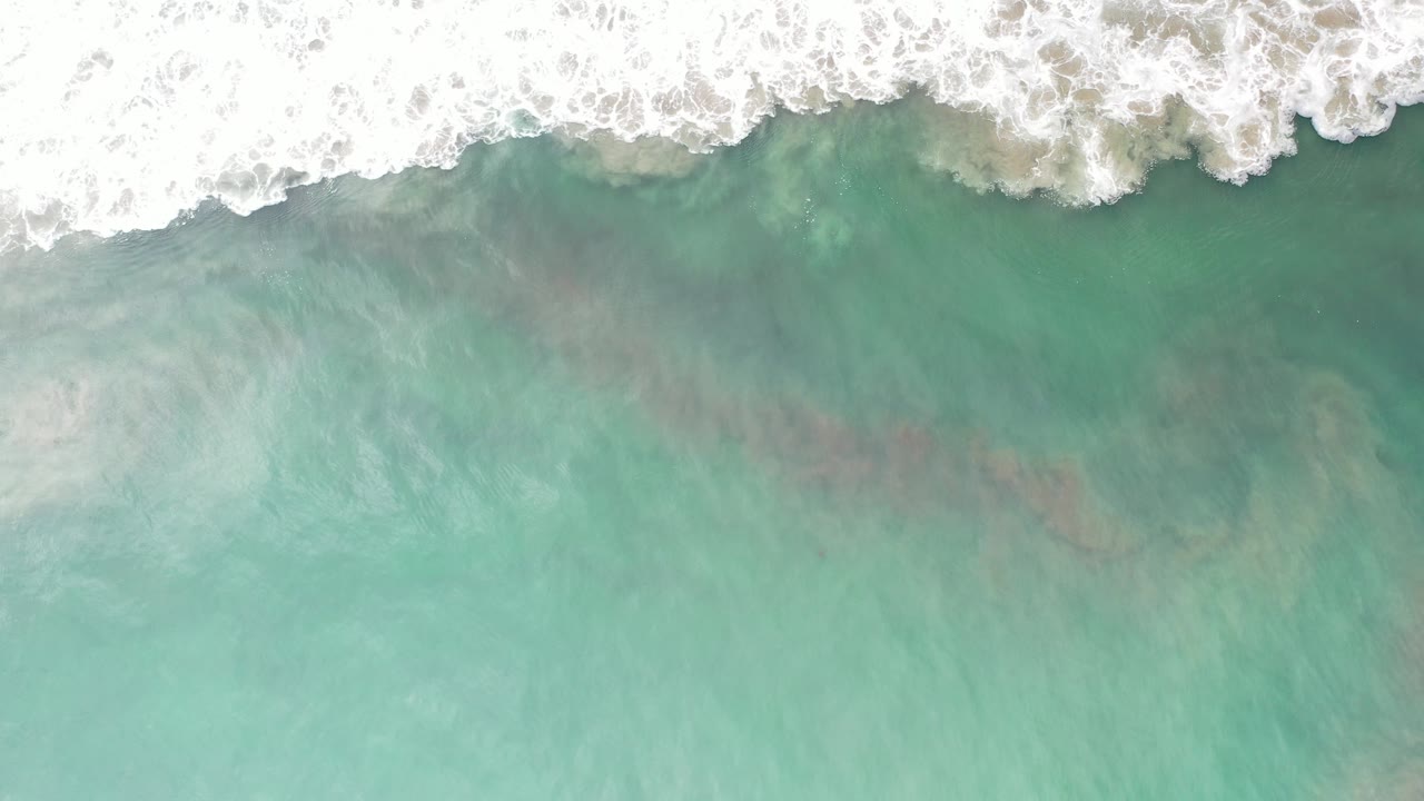 Overhead view of white surf foam along the top of frame over green-blue water in Los Cabos, Mexico, with no visible people.