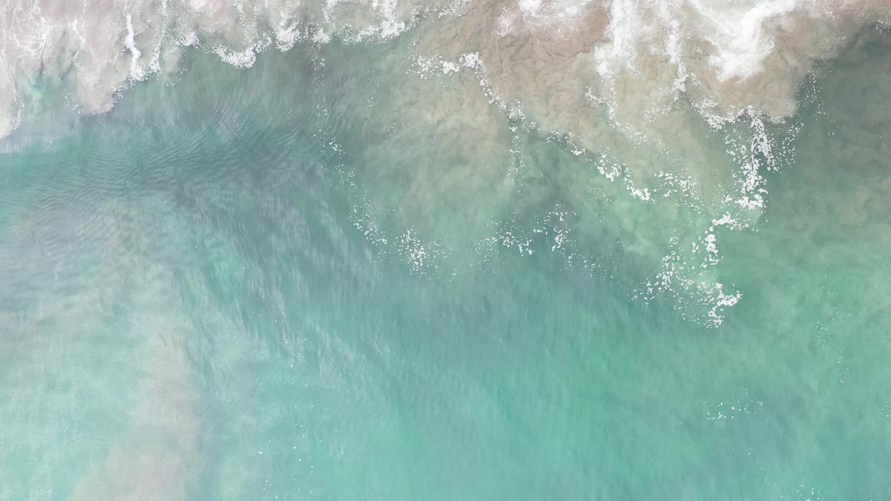 Overhead surf line with milky white foam over pale green water.