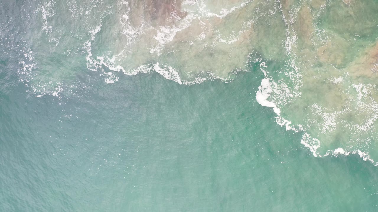 Turquoise ocean surface with white breaking water near rocky shallows.