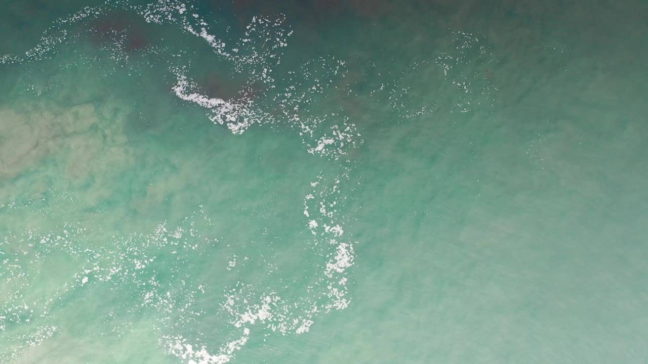 Aerial sea surface with white foam arcs over green-blue water.