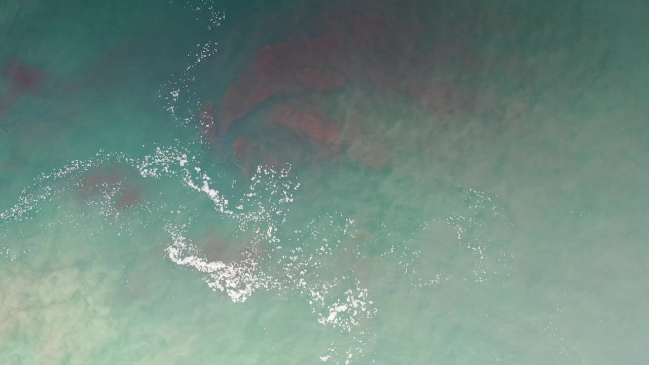 Turquoise water seen from above with foam glints and soft underwater color bands.