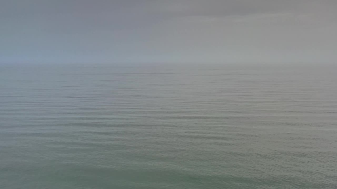 Los Cabos open water fills the frame with a faint horizontal horizon line, light haze overhead, low surface ripples, and no visible people.