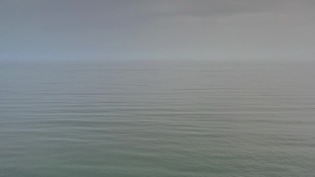 The Los Cabos water remains calm beneath a pale gray sky, with the horizon held steady and no visible people.