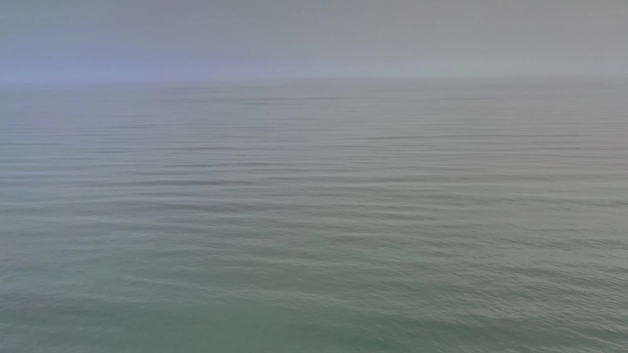 Blue gray ocean surface stretches to a soft cloudy horizon in Los Cabos, Mexico, with slightly darker water bands and no visible people.