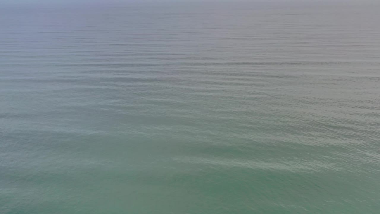 Muted green water in Los Cabos, Mexico shows a smooth upper band and faint ripple lines across the surface, with no visible people.