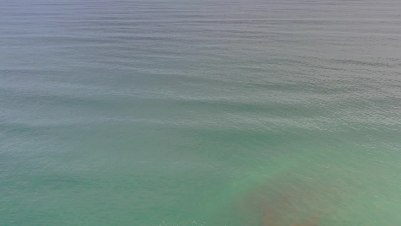 High-angle view of dim blue green water in Los Cabos, Mexico, with a muted wave band near the bottom and no visible people.