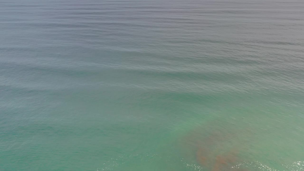 Blue green shallows with a low wave line and small foam flecks at the lower right.