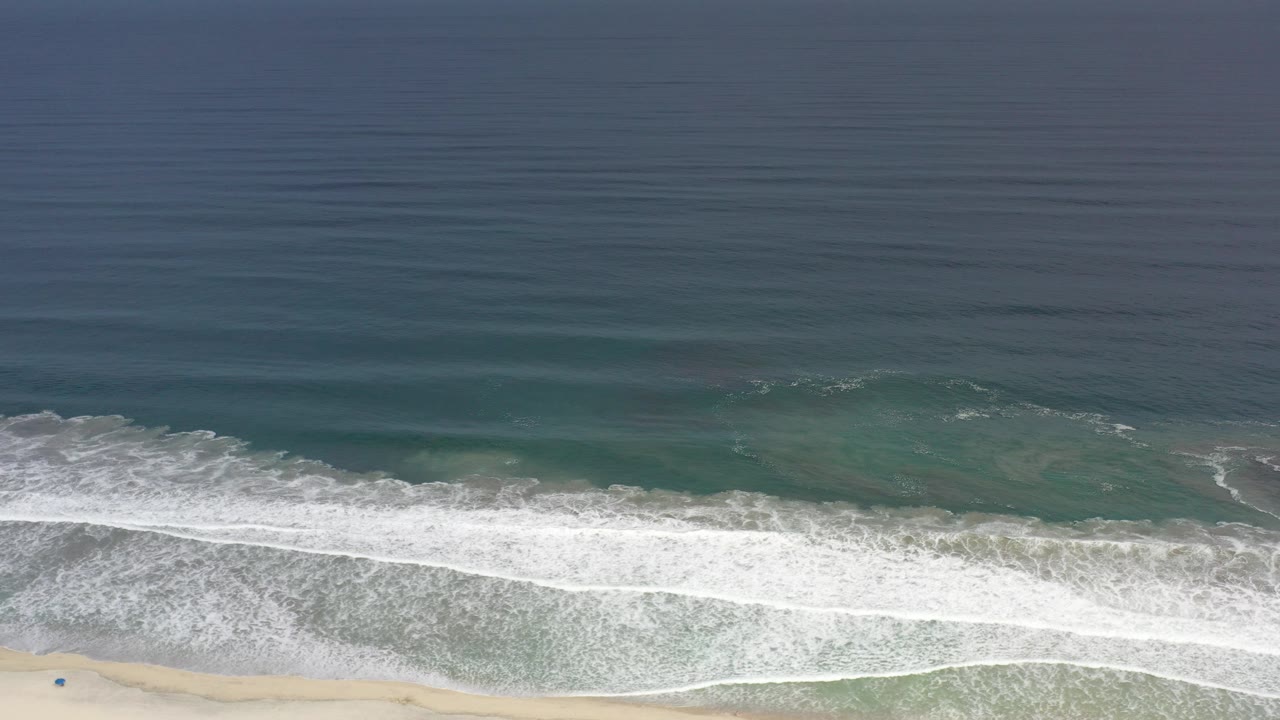 Aerial view of green ocean waves breaking onto a narrow sandy beach.
