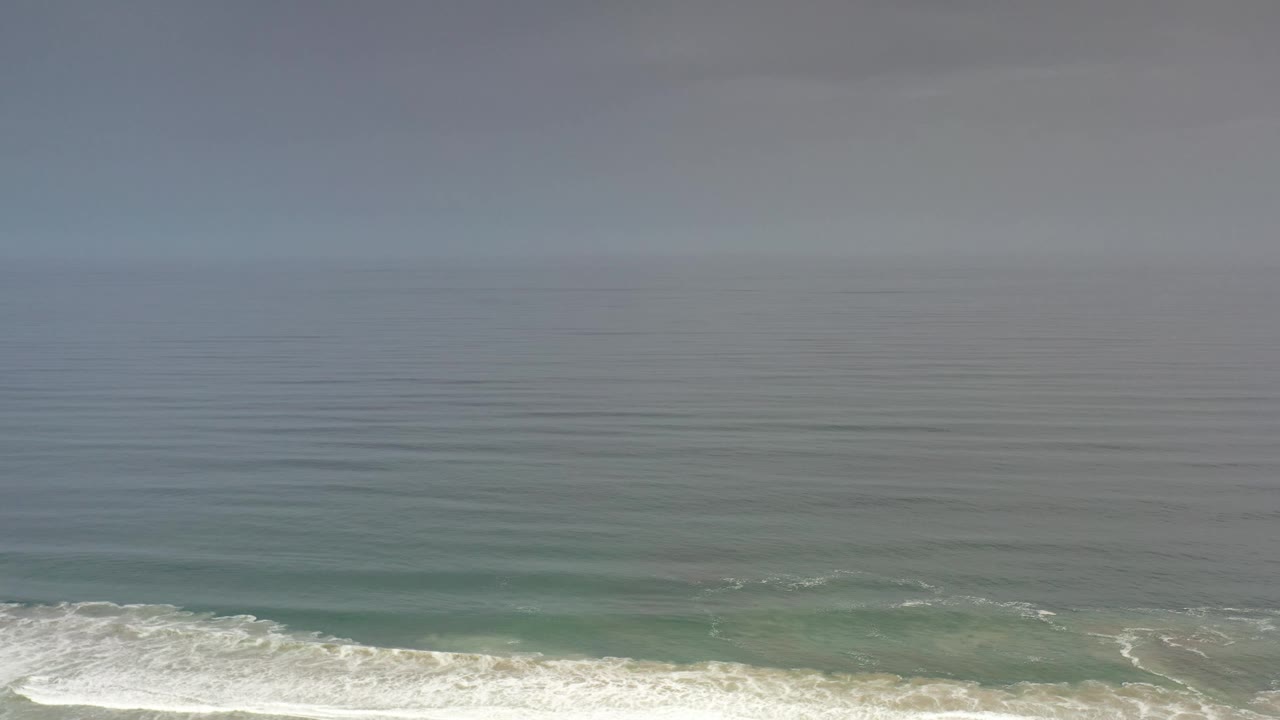 Aerial view of the Los Cabos ocean with evenly spaced surface ripples, white wave foam near the lower frame, and no visible people.
