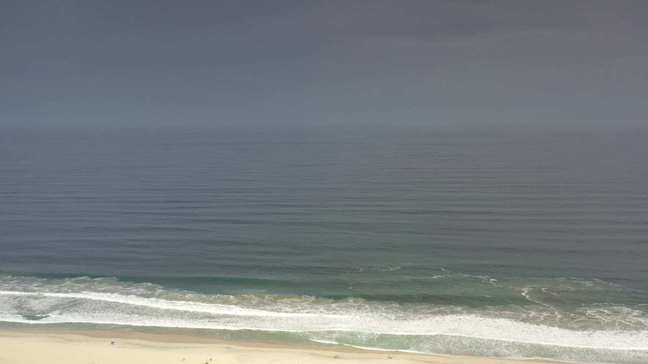 Aerial beach view with broad ocean and breaking surf.