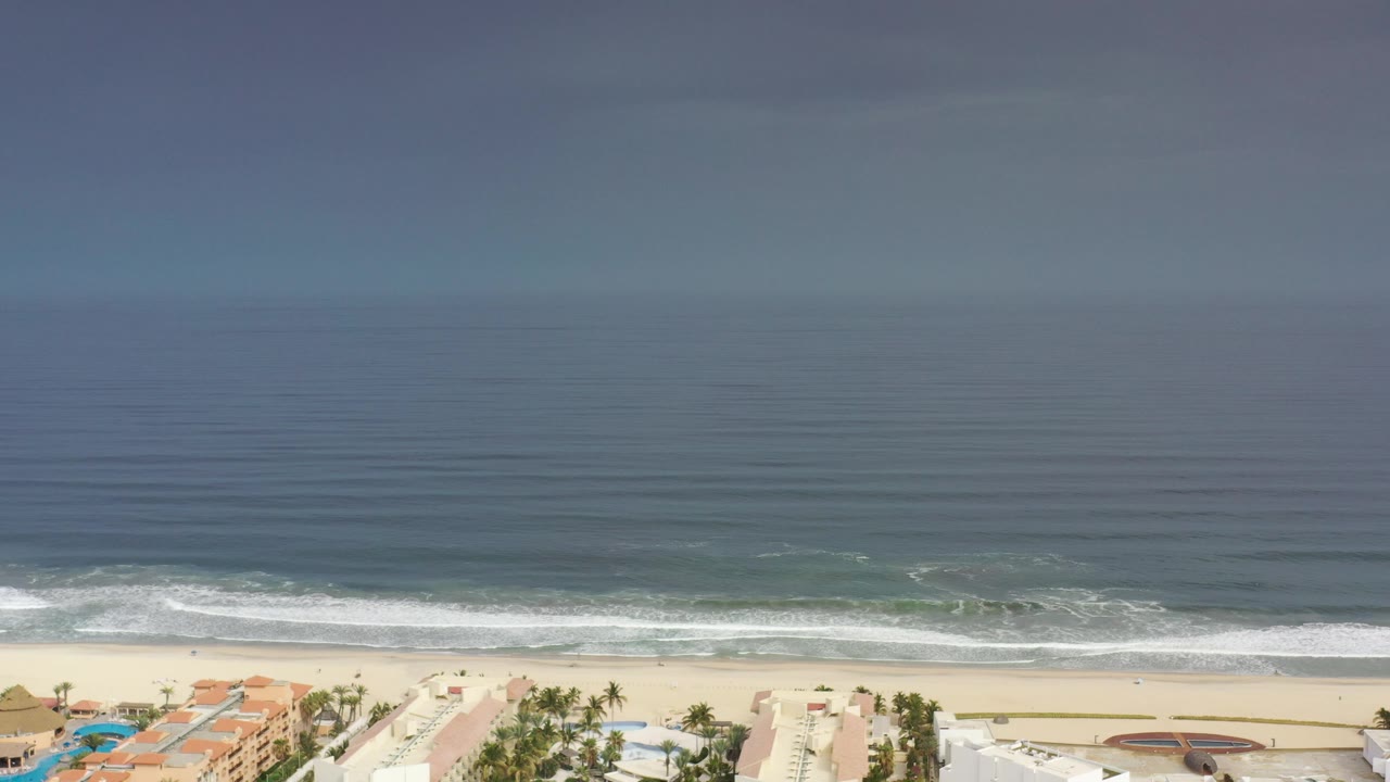 Hazy ocean view with waves breaking onto a beach and buildings below
