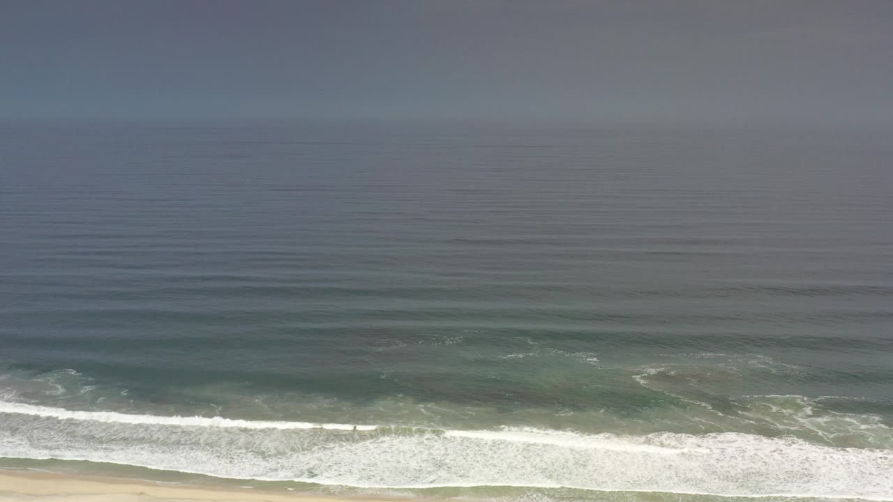 Elevated Los Cabos ocean view with white surf rolling toward a thin strip of sand and no visible people.