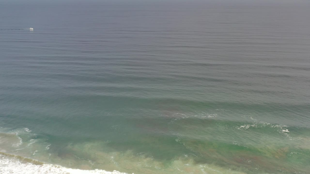 Green ocean with white shore break and a distant small boat