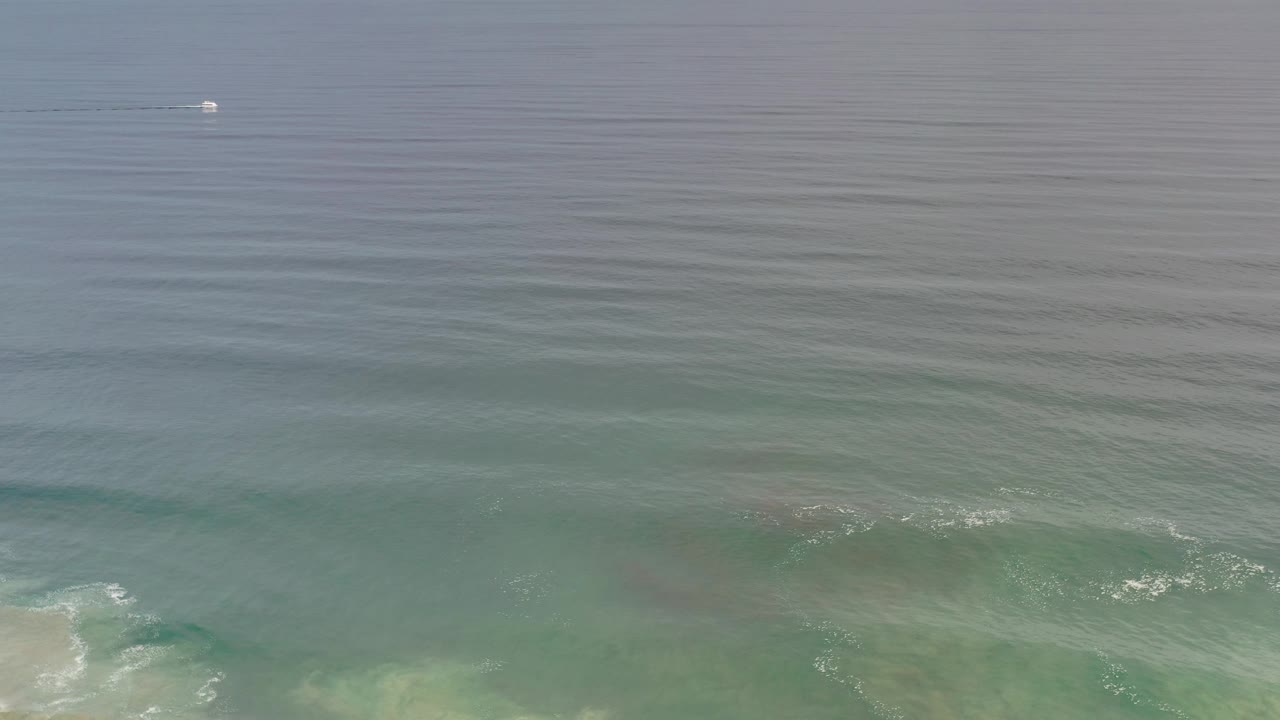 Boat near horizon over blue ocean and breaking shoreline surf