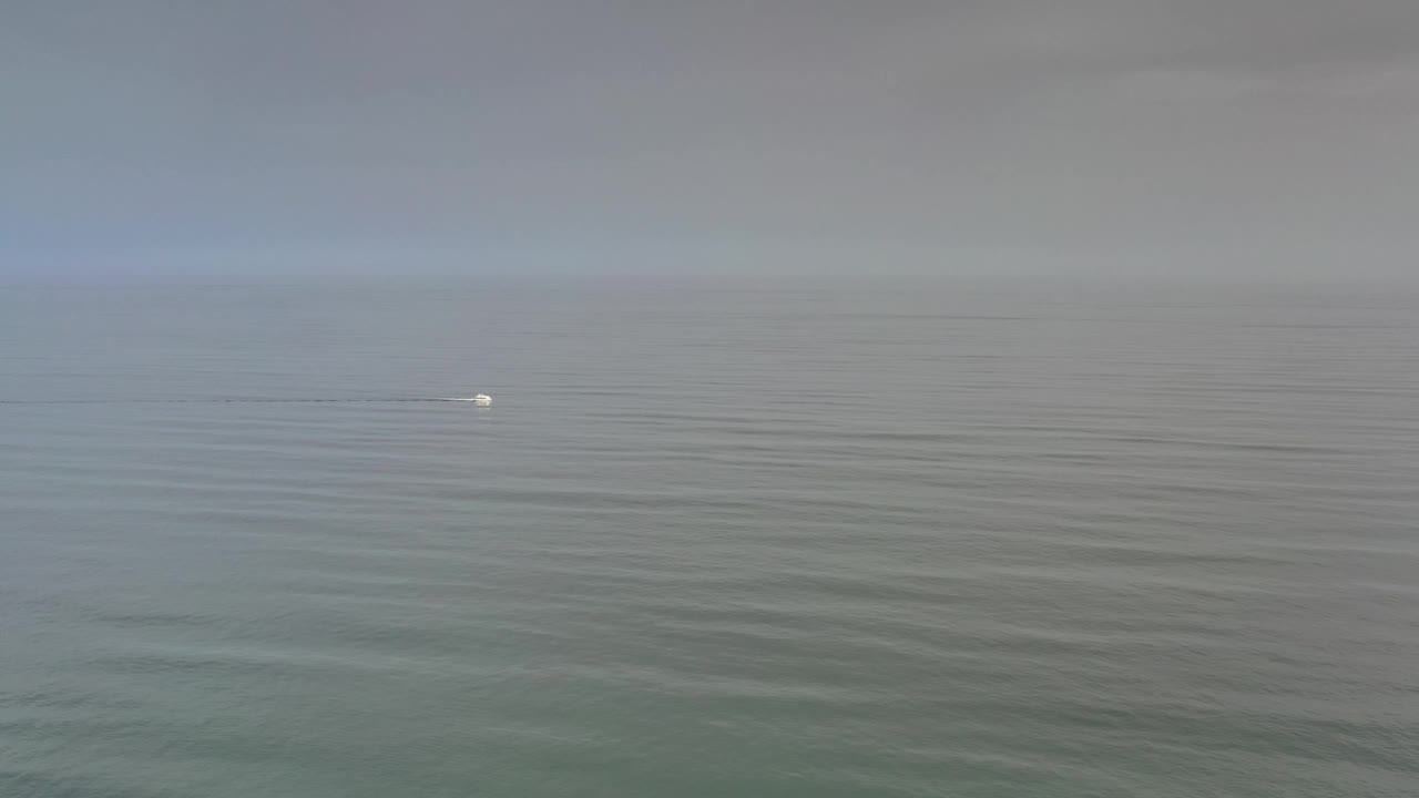 Los Cabos sea surface one second in, with the small white mark slightly brighter against layered ripples and a pale horizon, with no visible people.