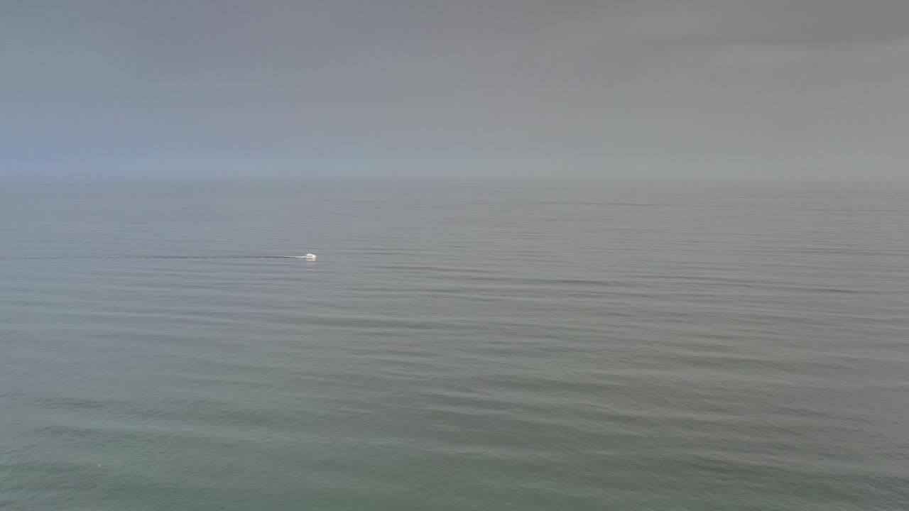 Open ocean and hazy horizon with a tiny white object on the water.