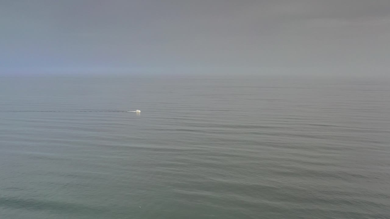 Wide Los Cabos ocean view under a hazy sky, with a small bright boat near the left side of the horizon and no visible people.