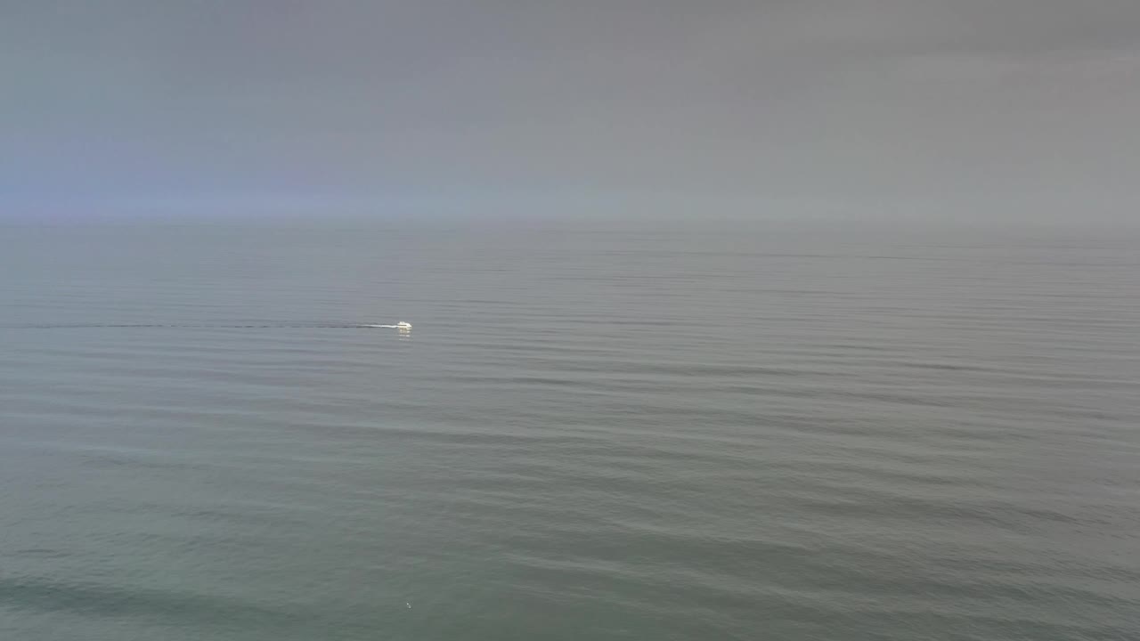 Los Cabos open water fills the frame as the small boat sits farther along the horizon line, leaving a thin wake with no visible people.
