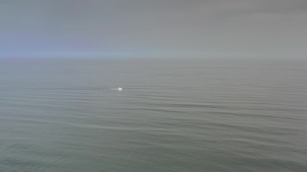 At the start of the Los Cabos clip, a small white boat sits left of center on open gray-green water beneath a wide cloudy sky, with no visible people.