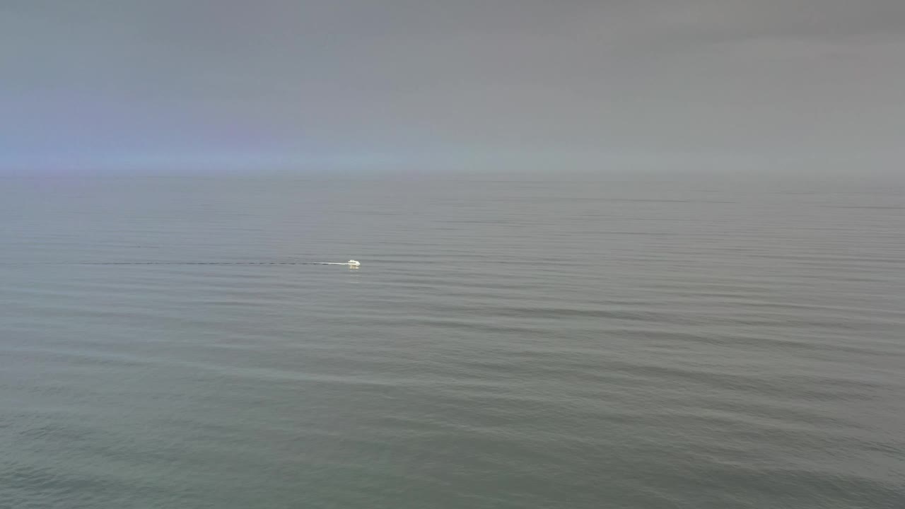 One second in, the small boat remains distant on the Los Cabos water, slightly farther across the frame against muted sea texture and cloud cover, with no visible people.