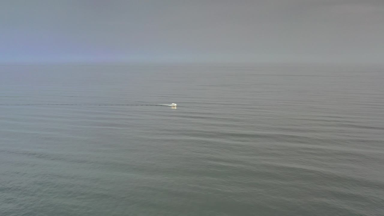 A small white boat crosses open blue-gray water in Los Cabos, Mexico, with a faint wake trailing behind it and no visible people.