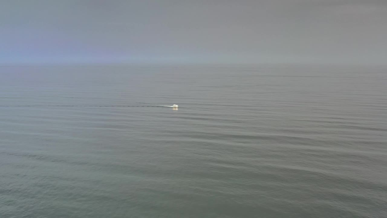 The white boat sits slightly farther across the open water, cutting a narrow pale wake through the rippled Los Cabos ocean with no visible people.