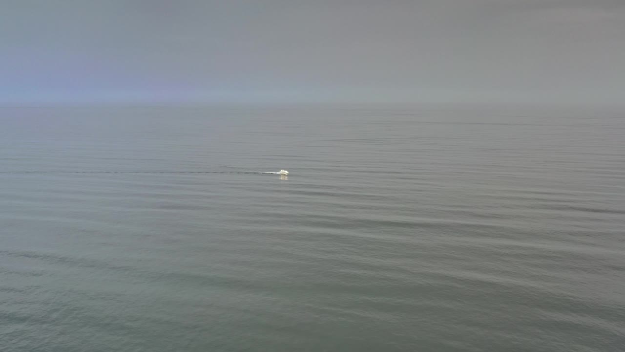 Distant white boat on calm dark blue ocean near a hazy horizon.