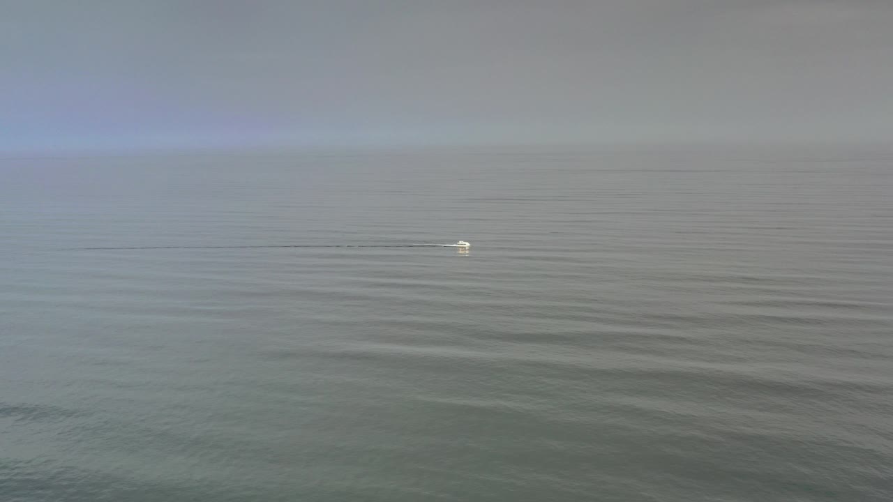 Foggy gray ocean with a small bright boat mark in the distance.