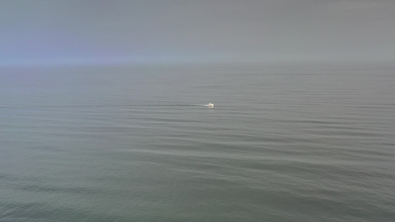 Wide Los Cabos ocean view at the start of the clip, with rippled green-blue water, a hazy horizon, a small bright distant surface mark, and no visible people.