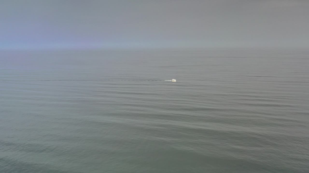 Small white boat on a hazy gray ocean horizon