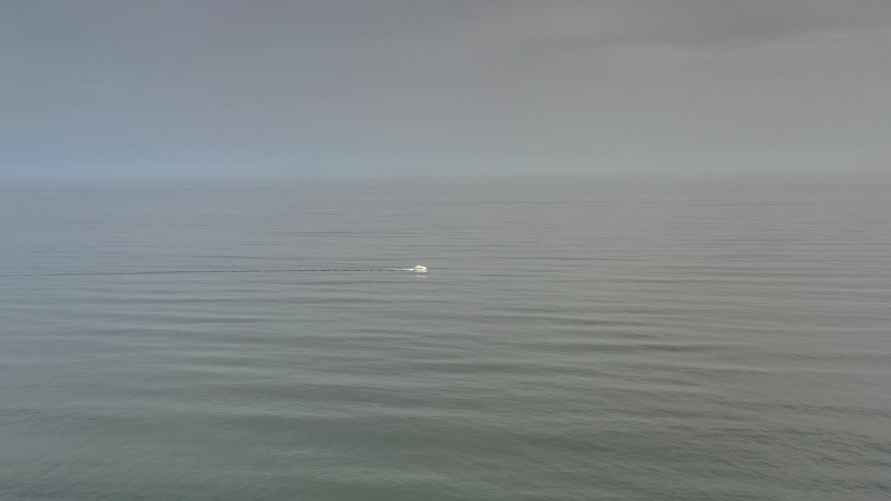 At the start of the Los Cabos clip, a small pale object floats near the center-left of open gray-green water beneath a flat hazy sky, with no visible people.